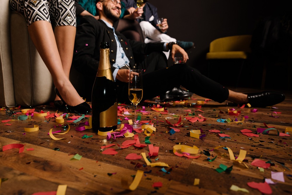 botella de champan y copa en suelo con confeti y gente de fiesta al fondo